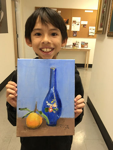 Young boy holding his painting of a blue decorative bottle with orange