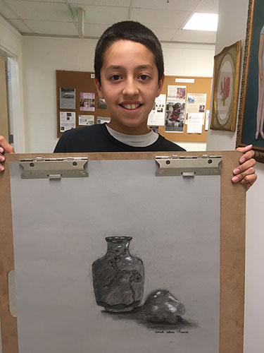 Young boy holding his charcoal drawing of a jar with fruit