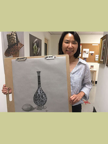 Young girl holding her charcoal drawing of decorative bottle with egg