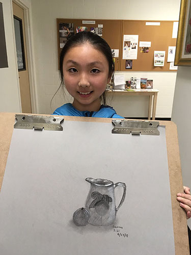 Young girl holding her charcoal drawing of a pitcher with fruit