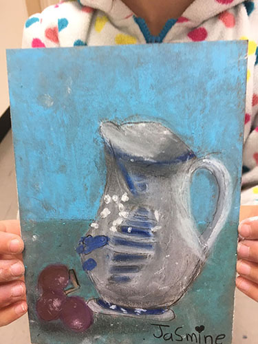 Young student Jasmine proudly holding her pitcher painting
